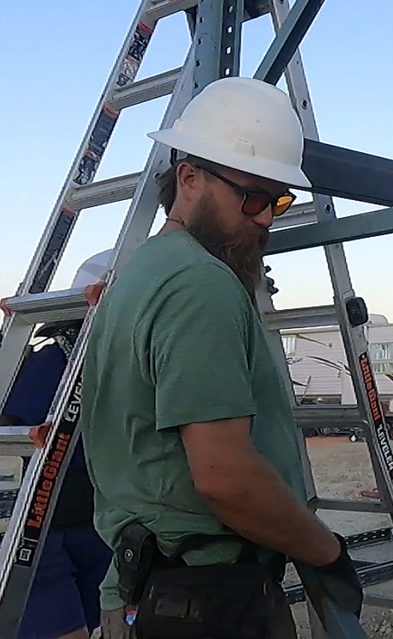 Kamas Valley Handyman owner in a white hard hat and sunglasses standing in front of a ladder