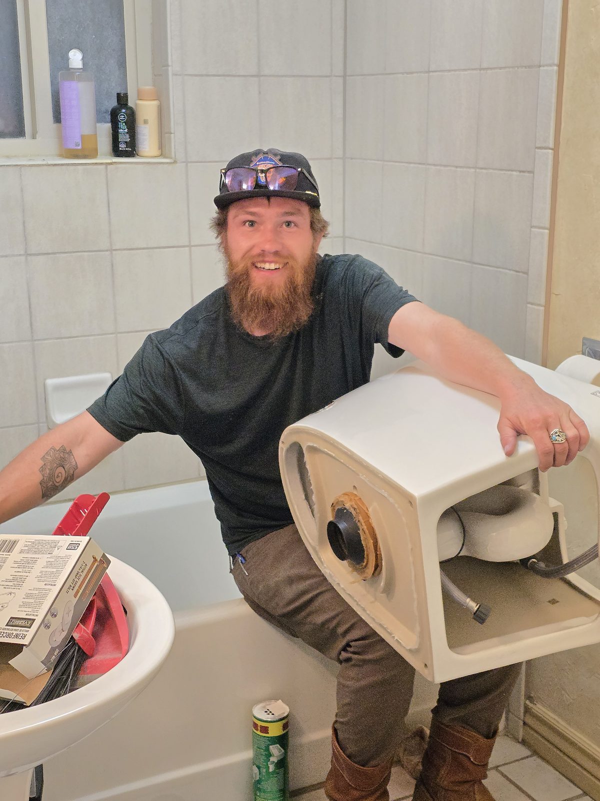 Kamas Valley Handyman smiling on a tub edge while holding an old toilet during a bathroom toilet swap